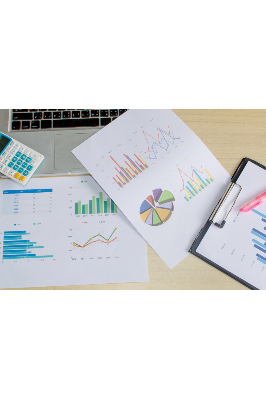 Diagramme und Grafiken auf einem Tisch, daneben ein Laptop und ein Clipboard.